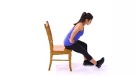 An exercise illustration shows a woman with a ponytail in black pants and a blue shirt sitting on a brown wooding chair. The woman's hand is on her waist, and she is bending forward as her leg extends in front of her. 
